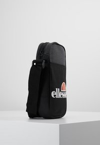 Borsa a spalla in tessuto nero con zip, parte superiore grigia e un logo bianco ben visibile. Manico regolabile singolo e forma rettangolare.