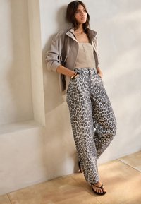 Jeans de pierna ancha con estampado de leopardo gris, camiseta ajustada beige, chaqueta gris claro con cremallera y chanclas negras. Texturas suaves y ajuste casual.