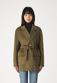 Abrigo de lana verde olivo con cuello de chal, cintura ceñida y dos bolsillos frontales; textura suave; corte relajado sobre un suéter de cuello alto negro.