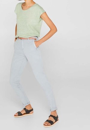 Jasnozielony top z krótkim rękawem, jasnoniebieskie wąskie spodnie z kieszeniami oraz czarne sandały z drewnianą podeszwą. Pasek w wzory.