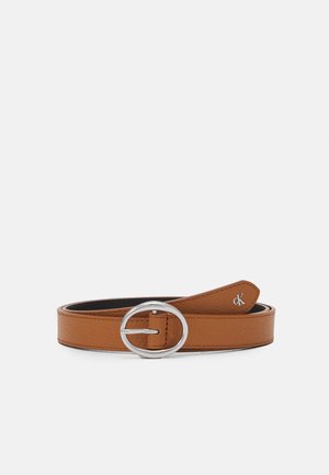 Bruine leren riem met ronde zilveren gesp en klein zilverkleurig cK-logo aan het uiteinde, plat gelegd op een witte achtergrond.