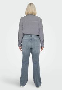 Camisa de manga larga a rayas en azul marino y blanco, combinada con jeans acampanados de un azul claro. La camisa tiene botones y un dobladillo redondeado; los jeans tienen bolsillos traseros.