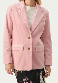 Rosa kordflockblazer med spetsiga slag, två framfickor och bruna knappar, matchad med en mönstrad, mörkblommig kjol.