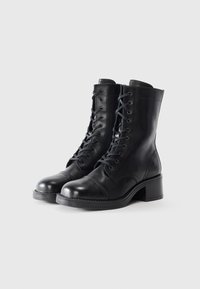 Schwarze Leder-Stiefeletten mit runder Zehenform, Schnürdesign und einem 2,5 Zoll Blockabsatz. Glatte Textur mit Nähdetails.