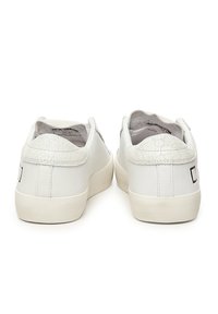 Sneaker bianche in pelle con un cappuccio sul tallone testurizzato e un design delicato. Il lato posteriore presenta una grafica minimale con accenti neri.
