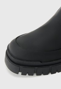 Bottine noire à la finition lisse et mate ; semelle en caoutchouc épaisse avec texture rainurée et motif de semelle distinct pour une meilleure traction.