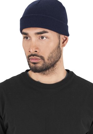 Navy ribbed knit beanie hat, featuring a snug fit and seamless crown. Worn with a black crew neck shirt.