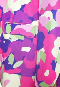 Primer plano de tela floral multicolor con flores rosas, moradas y blancas, y hojas verdes, que presenta un bolsillo con solapa rectangular cubierto de tela.