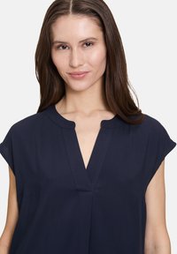 Marinebluse mit V-Ausschnitt und Kurzärmeln. Glatter, leichter Stoff; mit dezenten Nahtdetails am Ausschnitt und an den Seiten.