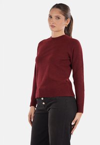 Maglione a maglia bordeaux con scollatura rotonda, maniche lunghe e vestibilità rilassata. Abbinato a pantaloni neri con dettagli in bottone dorato.
