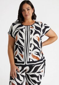 Schwarz-weiß gemusterte Bluse mit abstrakten Blattdesigns, mit bronzefarbenen Akzenten, kurzen Ärmeln und rundem Ausschnitt. Glatte Stofftextur.