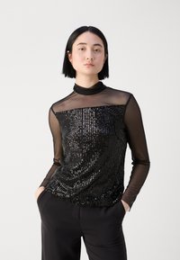 Schwarzes Paillettenoberteil mit einer taillierten Form und transparenten langen Ärmeln, ausgestattet mit einem hohen Kragen und einer glatten Textur. Kombiniert mit schwarzen Hosen.