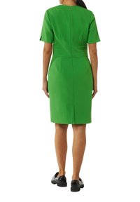 Zielona dopasowana sukienka z krótkimi rękawami, zamkiem błyskawicznym z tyłu i rozporkiem na dolnej części. Gładki materiał z dopasowaną sylwetką.