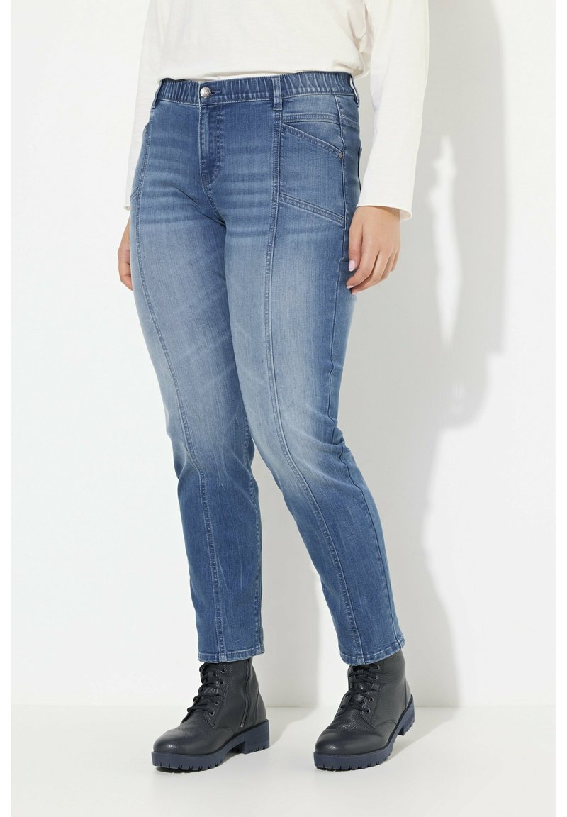 Siniset farkut, joissa on kapenevat lahkeet, teksturoitu pinta, joustava vyötärö, etutaskut ja nappikiinnitys.