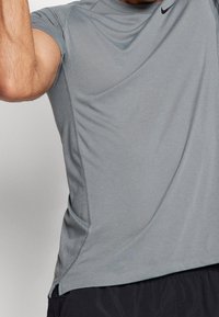 Harmaa urheilupaita, joka on valmistettu hengittävästä kankaasta. Sivukappaleissa on verkkopaneelit, ja rinnassa on pieni musta logo.