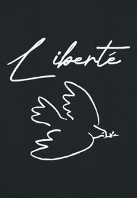 Un tissu noir présente le texte manuscrit blanc "Liberté" au-dessus d'un dessin linéaire d'un oiseau tenant une branche d'olivier, symbolisant la paix et la liberté.