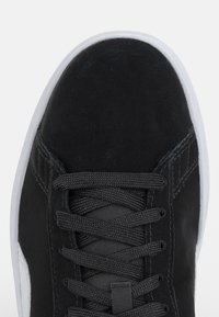 Zwarte suède sneaker met een afgeronde neus, gestructureerde veters en een contrasterende witte rubberen zool. Beschikt over subtiele stiksels en een zij-embleem.