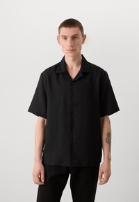 Camisa negra de manga corta hecha de tela texturizada, con un diseño frontal de botones y un cuello relajado. Estilo simple sin patrones.