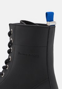 Bottine en cuir noir à finition lisse, dotée d'œillets argentés, de lacets noirs et d'une languette bleue à l'arrière. Logo embossé sur le côté.