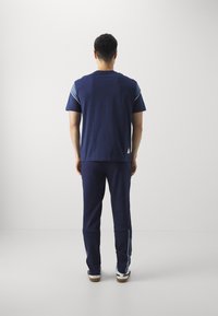 Navy tracksuit featuring a short-sleeve top and matching pants. The top has blue accents on the shoulders; smooth fabric, relaxed fit.