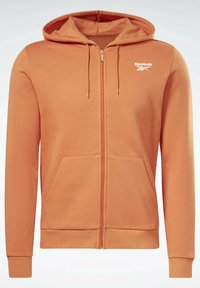 Sweat à capuche zippé orange avec poches avant, capuche à cordon, poignets côtelés et logo blanc Reebok sur la poitrine.