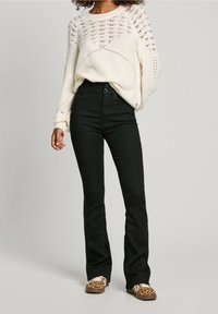 Pull tricoté blanc avec un motif ajouré aux épaules, associé à un pantalon noir taille haute et des chaussures à enfiler à imprimé animal.