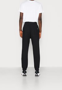 Svarta joggerbyxor med elastiska muddar, en bakficka och en avslappnad passform, kombinerat med en enkel vit t-shirt och svarta sneakers.