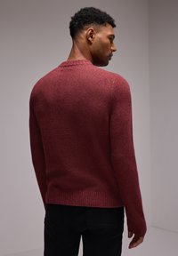 Pull en maille bordeaux avec un ourlet et des poignets côtelés, présentant un design texturé et un col rond. Modèle montré de dos.
