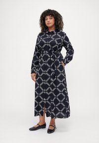 Abito navy a maniche lunghe con motivo geometrico bianco, colletto, vita sfiancata e tasche laterali. Presenta uno spacco all'orlo.