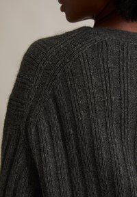 Donkergrijze gebreide trui met gestructureerde verticale strepen en een losse pasvorm, die een zachte, wolachtige stof en ribbelontwerp benadrukt.