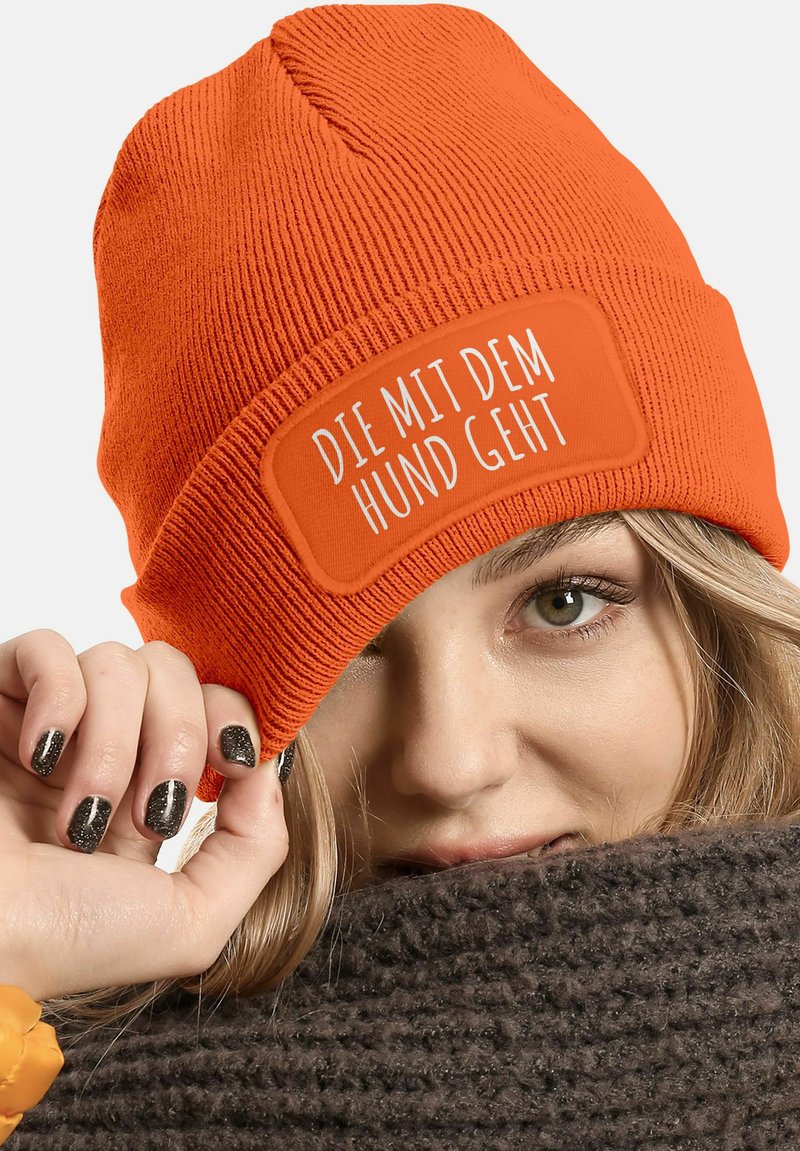 Orange knit beanie with a ribbed texture and a rectangular patch displaying white text. Warm fabric, snug fit, suitable for cold weather.