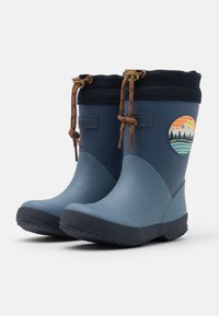 Bottes de pluie en caoutchouc bleu avec une semelle noire texturée, un revers bleu foncé et un cordon brun. Présente un patch sur le thème de la montagne sur le côté.