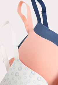 Tres sujetadores en colores variados: un azul marino, un rosa suave y uno blanco con un estampado floral azul. Las tirantes están hechas de una tela suave.