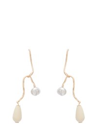 Guldtonade örhängen med en vågig design, som har klara glaskulor och vita keramikdetaljer. Texturerad yta ökar det visuella intresset.