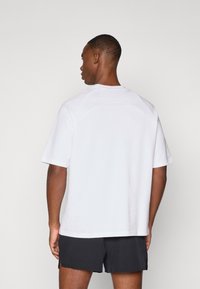 Camiseta blanca de manga corta con mangas raglán, escote redondo y un corte relajado, hecha de una mezcla de algodón. Vista trasera mostrada.