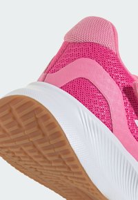 Baskets de sport roses avec tige en mesh, semelle en caoutchouc et intercalaire blanc. Présente des motifs texturés et un détail de logo sur le côté.