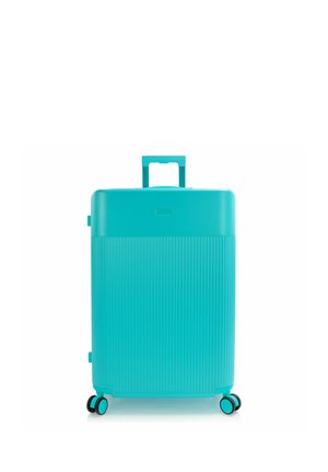 Maleta rígida turquesa con ranuras verticales, cuatro ruedas giratorias y un asa retráctil extendida.