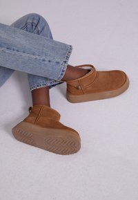 Botine din velur maro, cu căptușeală pufoasă, vârful rotund și o talpă din cauciuc ușor masivă, având un model în herringbone.