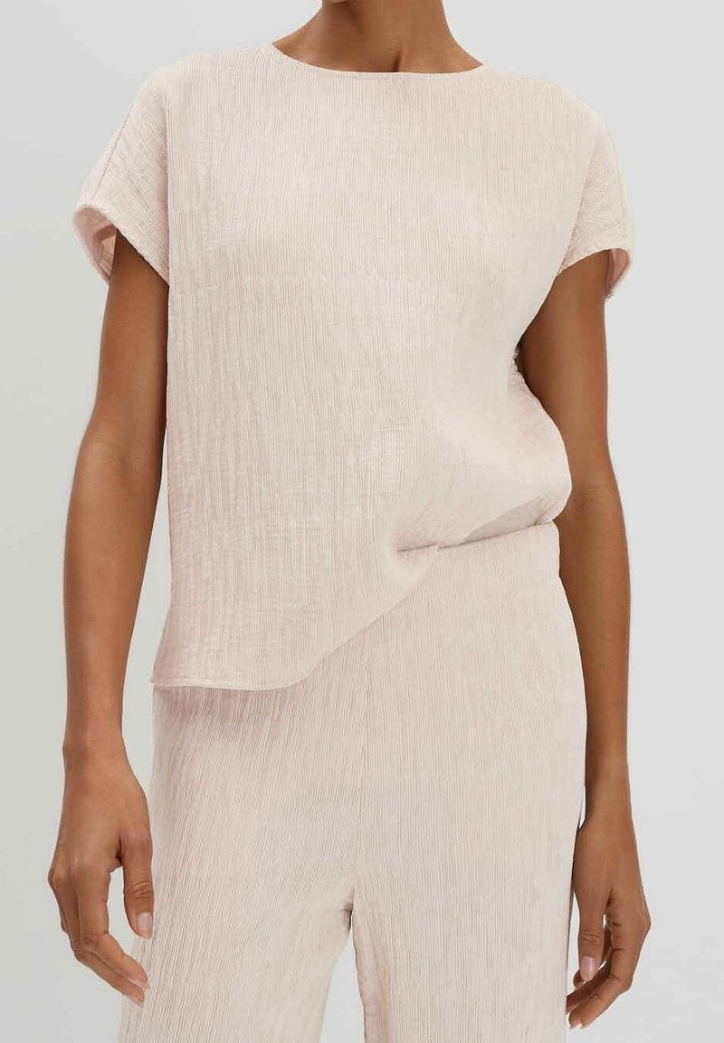 Femme portant un haut texturé beige clair à manches courtes et un pantalon assorti ample avec un col rond.