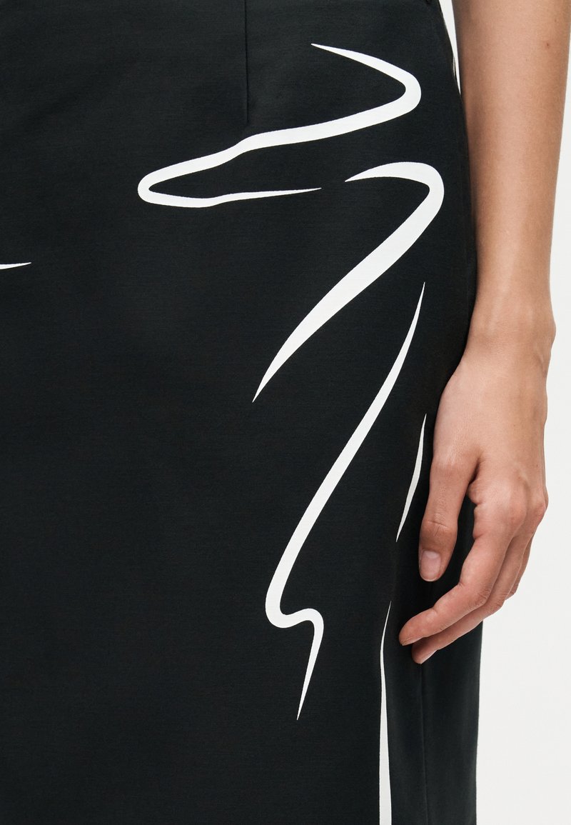 Close-up of a person's hand resting beside a black skirt with abstract white zigzag patterns.