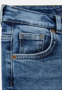Jeans in denim con un lavaggio blu sbiadito, cuciture dorate e una piccola tasca frontale, caratterizzati da un rivetto in metallo marchiato e un taglio classico.