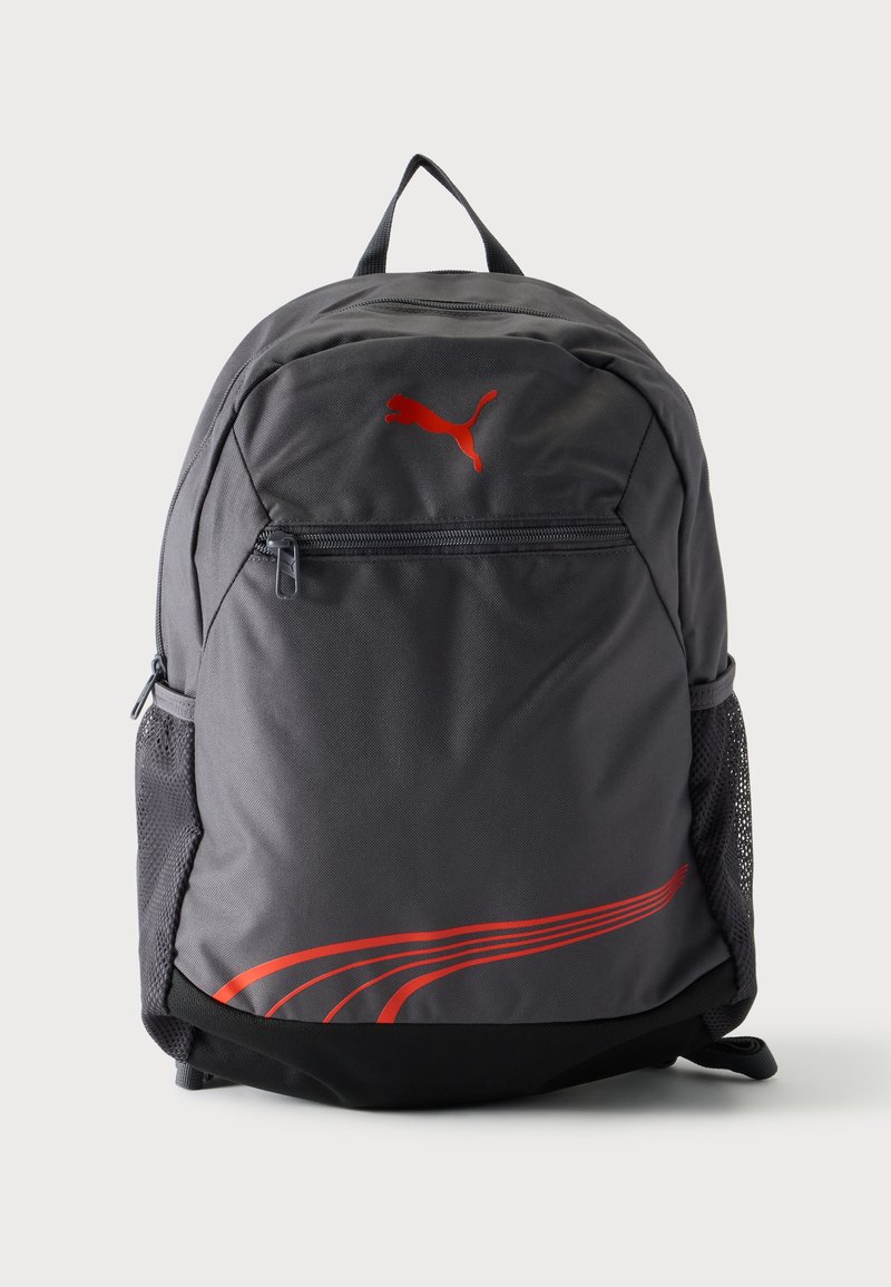 Σκούρο γκρι σακίδιο πλάτης Puma με κόκκινο λογότυπο και ρίγες, μπροστινή τσέπη με φερμουάρ και δίχτυα στα πλαϊνά, όρθιο σε λευκό φόντο.