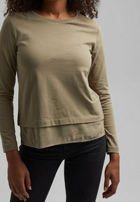 Langärmliges, olivgrünes Oberteil mit rundem Halsausschnitt, geschichteten Saum und weichem, strukturiertem Baumwollmaterial, kombiniert mit dunklen Jeans.