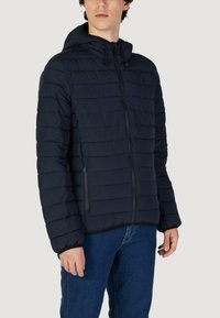 Giacca bomber navy con design a righe orizzontali, cappuccio, zip frontale e due tasche laterali con zip. Il materiale sembra leggero e isolato.