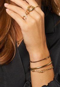 Anillos y pulseras de oro que presentan texturas variadas, incluyendo diseños lisos, retorcidos y enlazados, con acentos en marrón y oro.