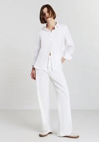 Weißes Hemd mit Kragen, kombiniert mit weiten weißen Hosen. Beide Kleidungsstücke haben eine glatte Textur und ein lässiges Design.