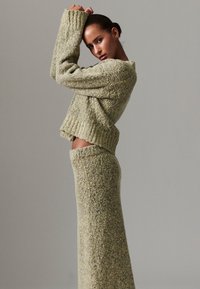 Dvodijelni pleteni komplet od mekanog, teksturiranog materijala s kratkim džemperom širokih rukava i dugom suknjom u prigušenim zelenim tonovima.