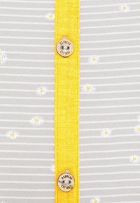 Šedá pruhovaná košile s žlutým knoflíkovým páskem, se vzorem bílých sedmikrásek. Na knoflíku je vygravírované "Ragwear EST 1997".