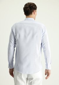 Camicia a maniche lunghe di colore azzurro chiaro con tessuto strutturato, polsini con bottoni e orlo curvo. Presenta un colletto classico e un dettaglio sulla spalla posteriore.
