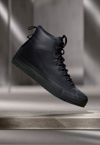 Zwarte hoge sneakers van gestructureerd leer, met ronde veters, een gladde zool en een rubberen neuskap met een ruitpatroon.